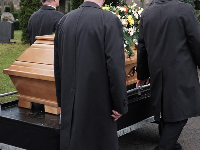 Trauerzug mit Sargträgern auf dem Weg zur Grabstätte während einer würdevollen Erdbestattung in Bischofsheim auf einem Friedhof.