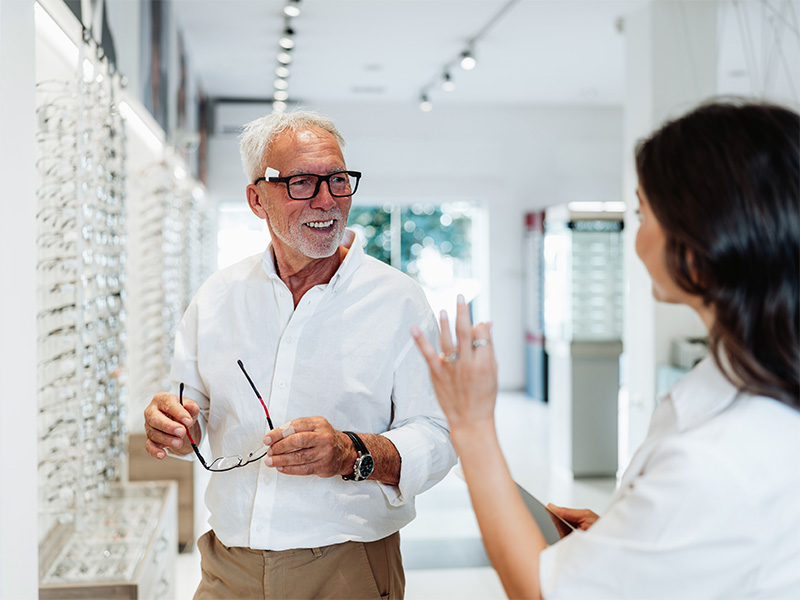 Augenoptiker in Hochheim berät einen älteren Kunden bei der Auswahl einer passenden Brille und zeigt verschiedene moderne Brillenfassungen.
