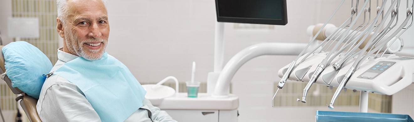 Älterer Mann sitzt entspannt im Zahnarztstuhl und lächelt zufrieden nach erfolgreicher Behandlung mit Zahnimplantaten in moderner Praxis