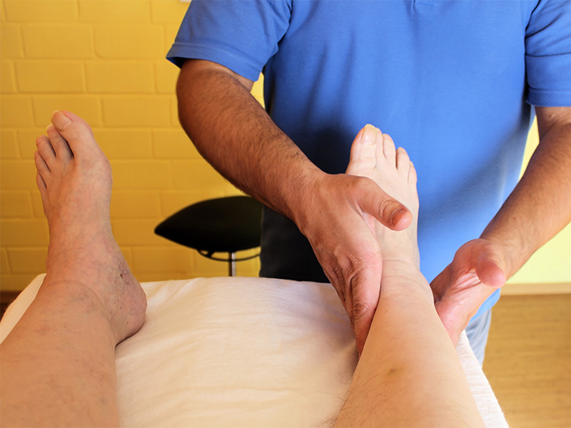Lymphtherapeut führt manuelle Lymphdrainage an Bein einer Patientin zur Unterstützung des Lymphabflusses und Reduktion von Schwellungen durch.