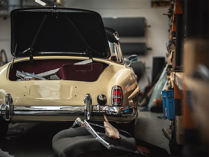 Mehrere Oldtimer in Rüsselsheim während der Restaurierung in einer Fachwerkstatt mit Hebebühnen, Werkzeugen und sorgfältigen Karosseriearbeiten.
