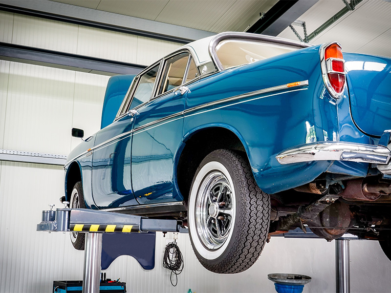 Blauer Oldtimer auf einer Hebebühne in einer Oldtimerwerkstatt in Rüsselsheim während professioneller Wartungs- und Restaurierungsarbeiten.