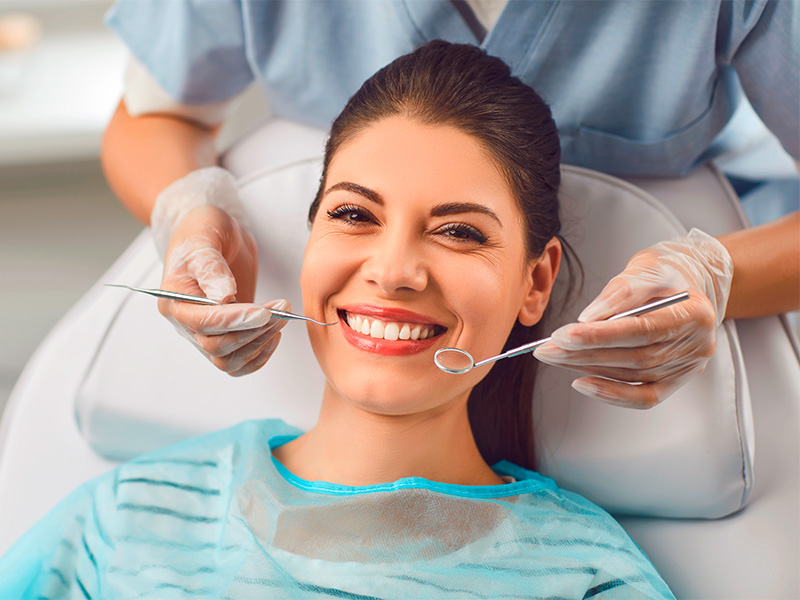 Zahnarzt untersucht Zähne einer lächelnden Patientin während Behandlung im Bereich Oralchirurgie in Mainz in moderner Praxis.