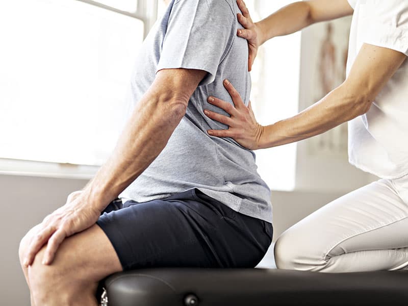 Physiotherapie bei Rückenschmerzen in Mainz: Therapeutin behandelt Patient im unteren Rückenbereich.