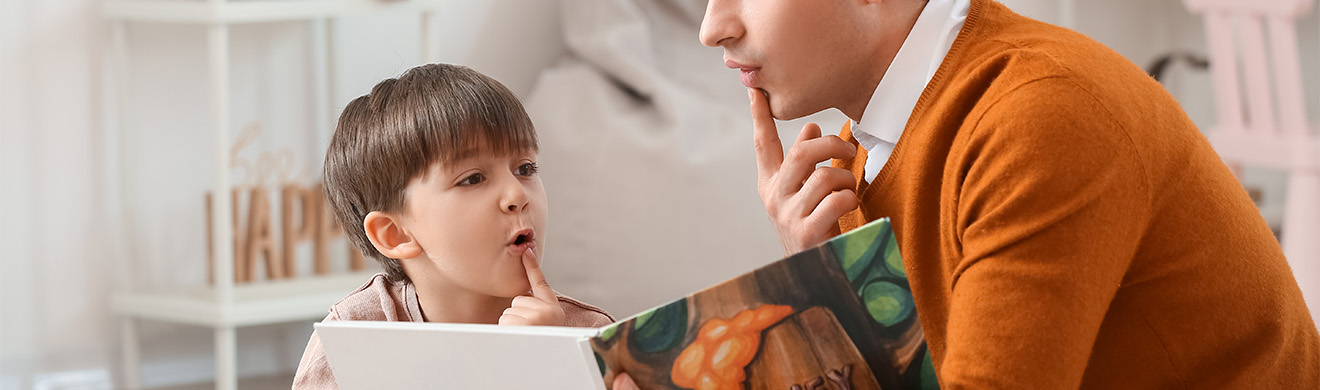 Logopäde unterstützt kleinen Jungen beim Lesen eines Buches im Büro, fördert Sprache und Kommunikationsfähigkeiten.