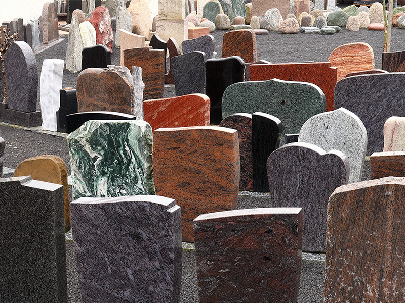 Grabsteine aus Granit in verschiedenen Formen auf Ausstellungsgelände eines Steinmetzbetriebs mit Natursteinmustern