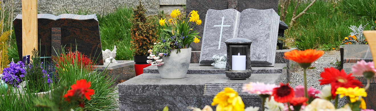 Graniturne und Grabsteine in Buchform auf gepflegtem Grab mit dekorativer Bepflanzung und Blumenarrangement